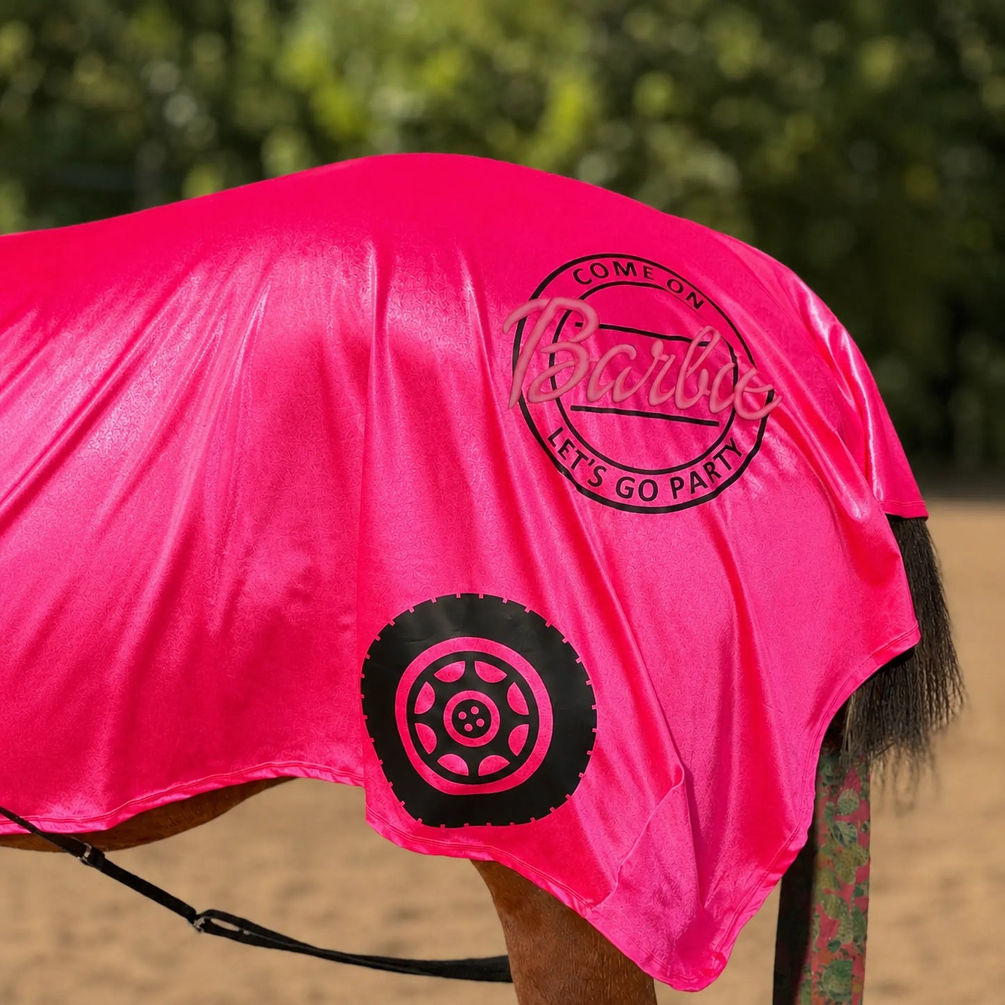 Horse wearing a bright pink barbie costume rear view with text and a tire graphic on a natural background
