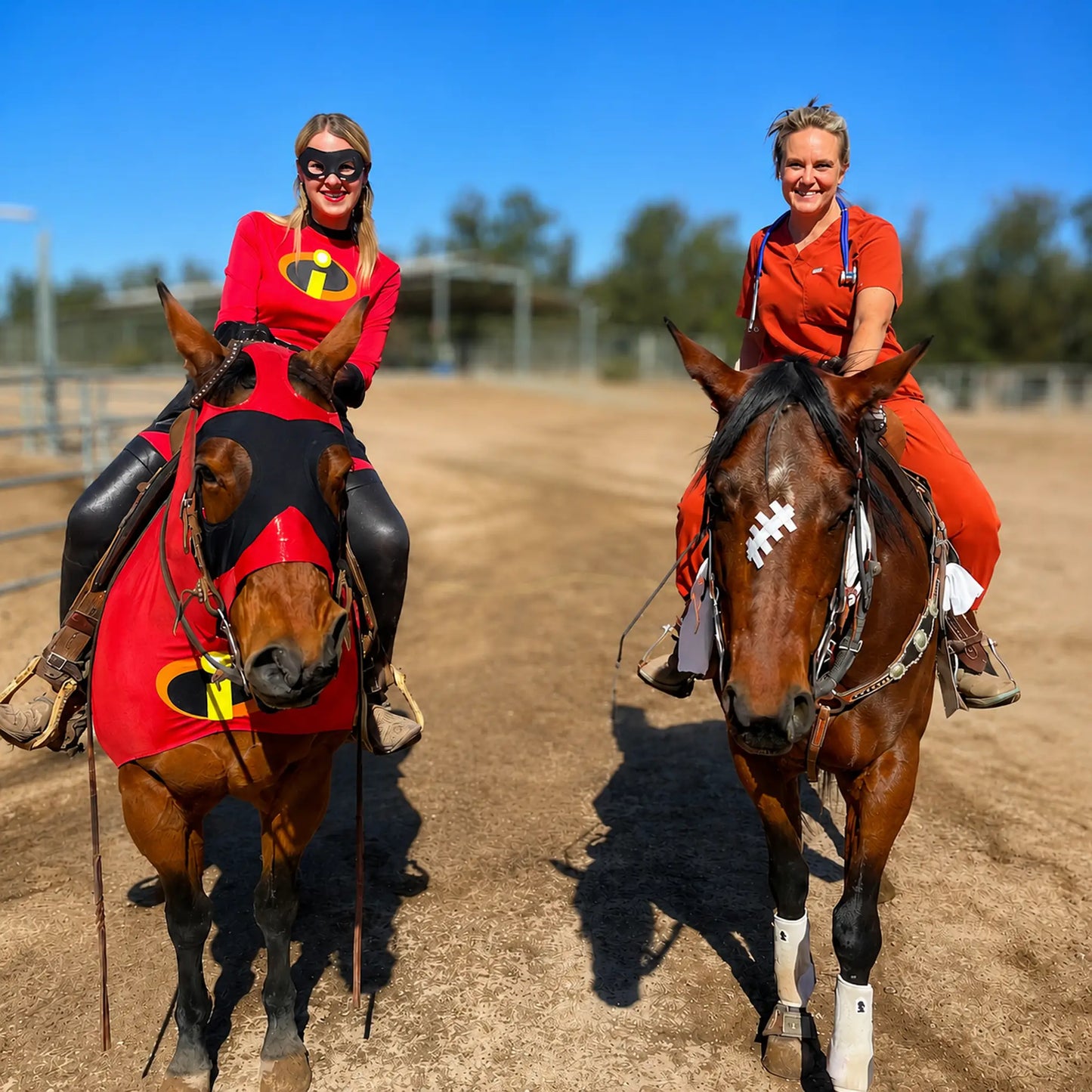 Two women in superhero metallic red incredibles sleazy costume riding horses on a dirt track.