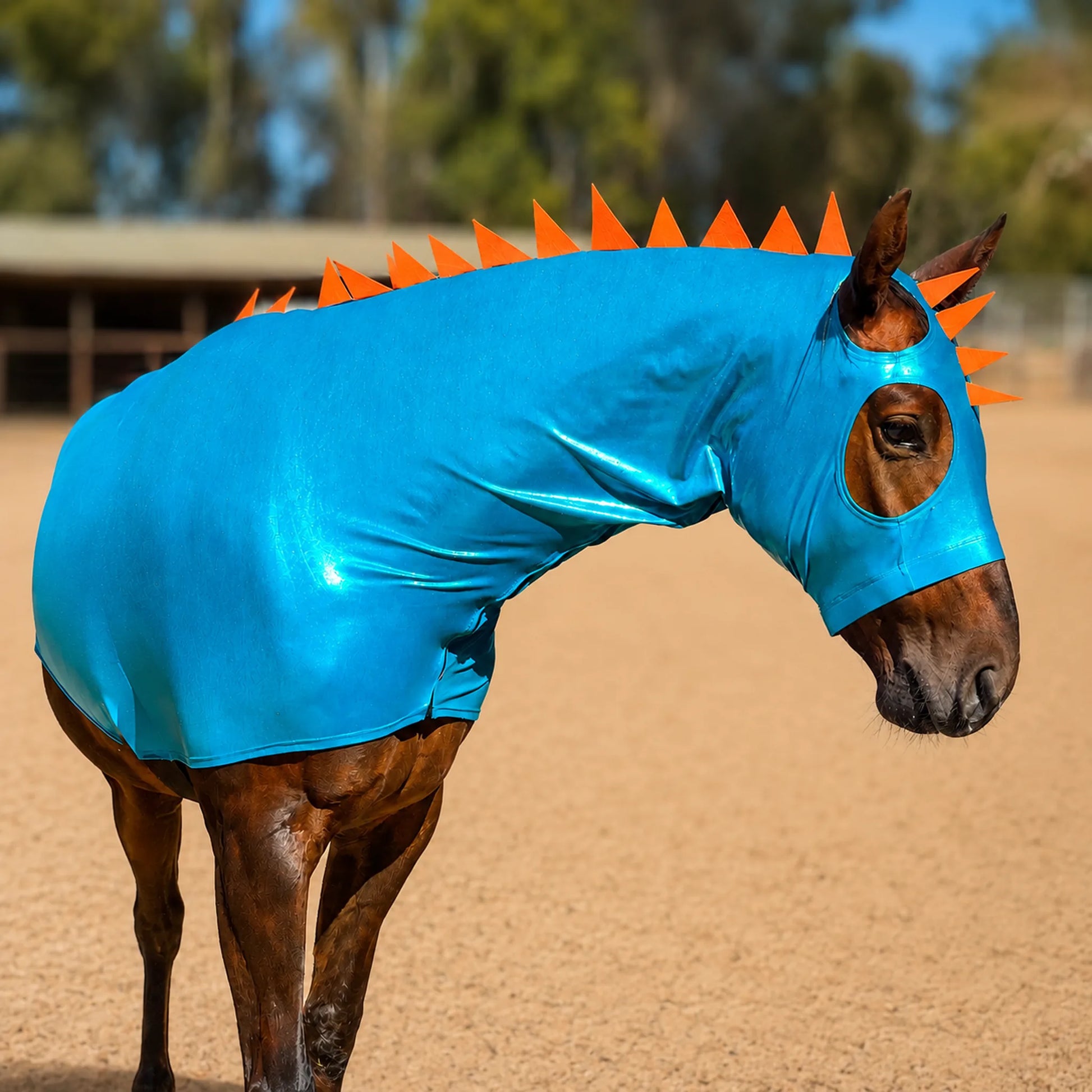 Horse wearing a metallic blue dragon costume with orange spike costume and matching tailbag in an outdoor setting
