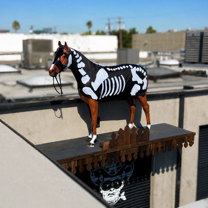 Horse wearing a skeleton costume sleazy on a rooftop with buildings in the background