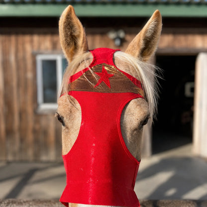 Horse wearing a red Wonder Woman horse costume hood sleazy with a star design in front of a wooden building.