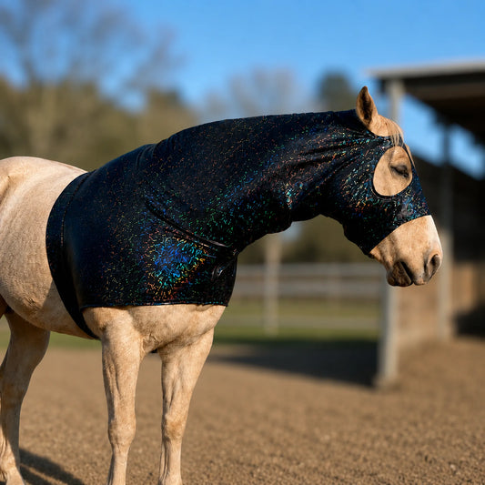 A light-colored horse standing in an outdoor stable wearing a shiny hologram black horse sleazy hood with a holographic, iridescent sparkle effect.