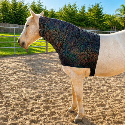 Horse wearing a shiny hologram leopard faceless hood sleazy in an outdoor setting with greenery.