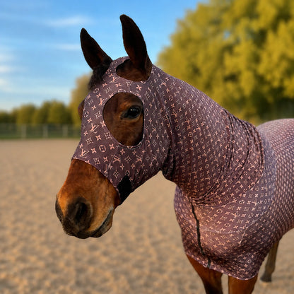 A horse wearing a LV brown full body sleazy in an outdoor paddock with trees and sky in the background.
