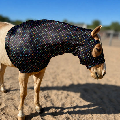 A light-colored horse standing in a sandy outdoor arena wearing a fitted LV color sleazy hood right side view.