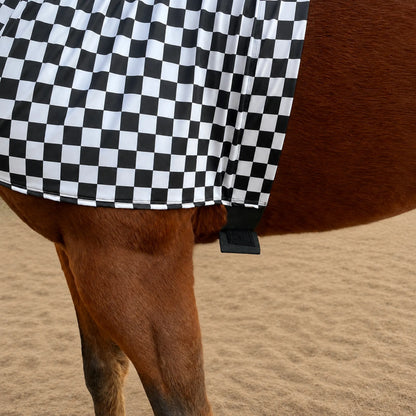 A close-up of a brown horse wearing a black and white checkered sleazy hood belly view, standing on a sandy ground.