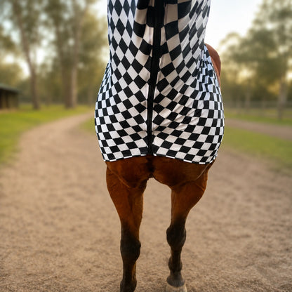A close-up rear view of a horse wearing a black and white checkered sleazy hood chest view on a dirt path outdoors.