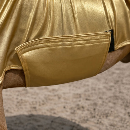 Close-up of a shiny metallic gold full body sleazy, with the horse's tan legs visible at the sides and a sandy ground in the background.