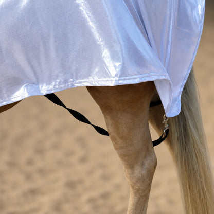 Close-up of a horse's leg strap wearing a shiny metallic  silver full body sleazy with black straps and metal hardware, set against a sandy arena background.