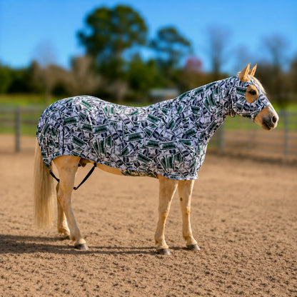 A light-colored horse standing in a sandy outdoor arena wearing a patterned horse money full body sleazy. The sleazy features a repeating green and black money abstract pattern on a white background.